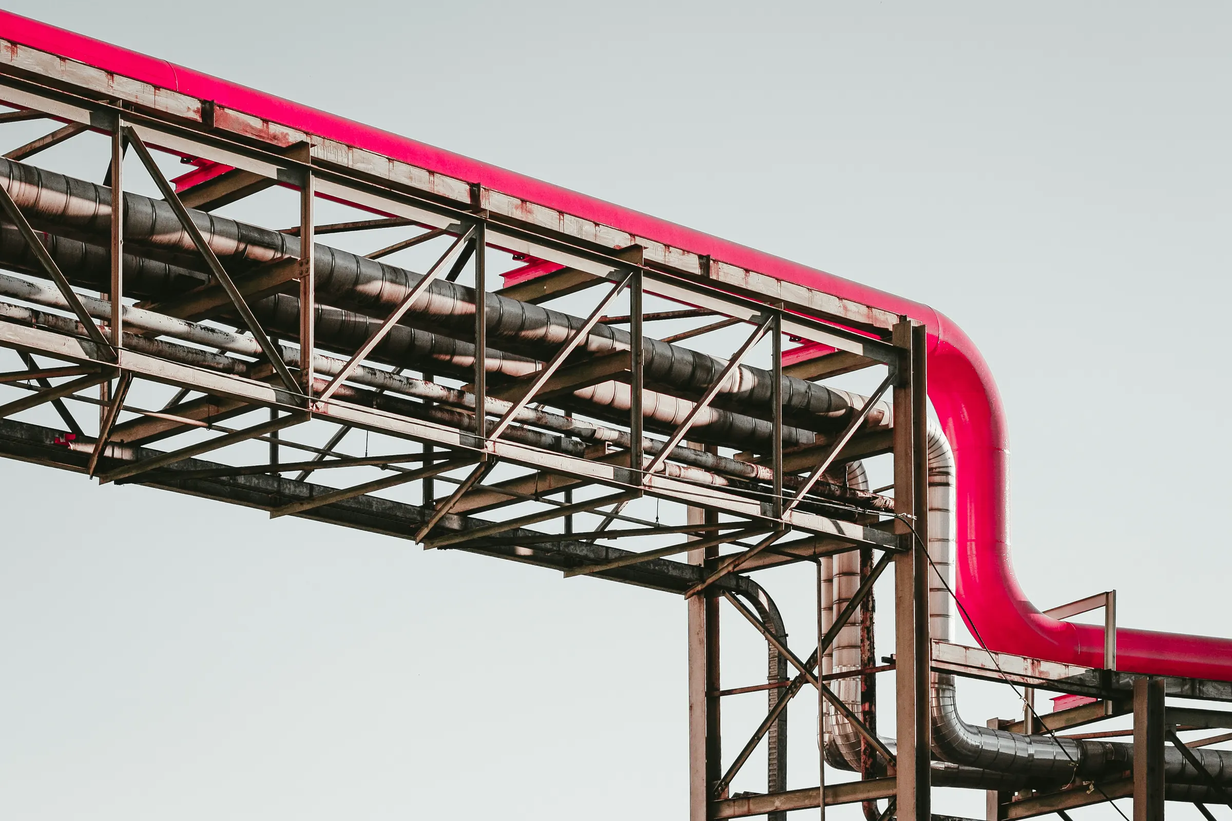A pipe rack carrying insulated process lines across an overhead steel bridge.
